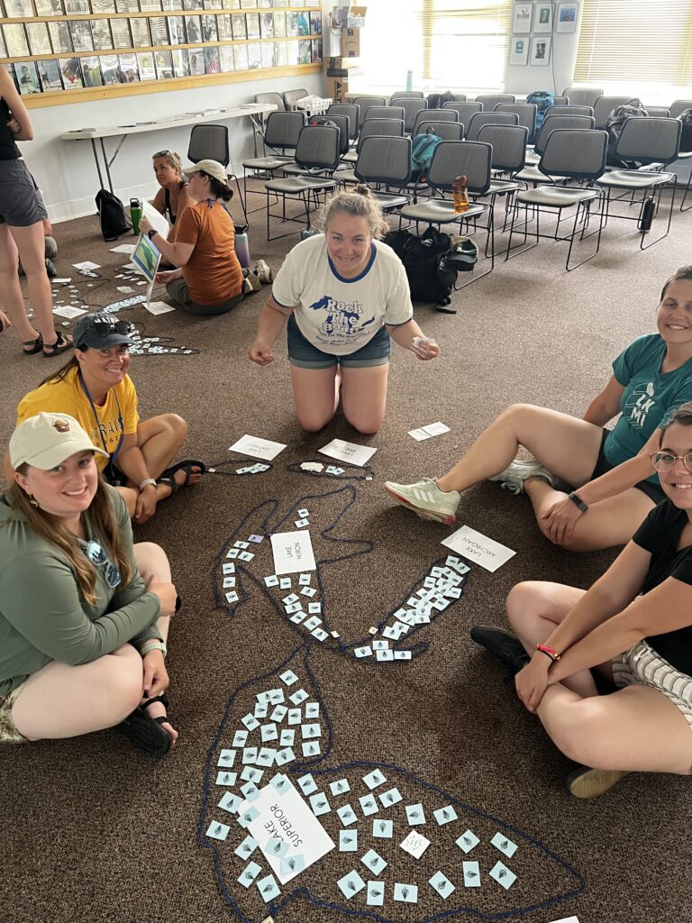 Five educators sit on the floor working on a Great Lakes lesson. Educators explore water quantity and commercial fishing.