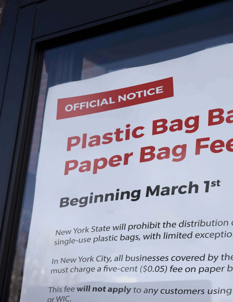 A sign on a window of a grocery store noting the plastic bag ban in NY