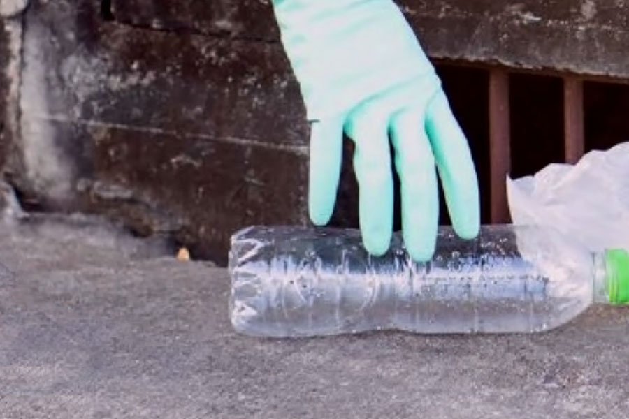 A person picks up a plastic bottle that is next to a street drain