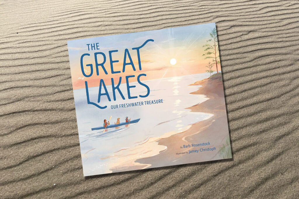 Book Cover of the The Great Lakes Our Freshwater Treasure includes a beach shoreline with trees in the distance, two people canoeing with a dog , and the sun near the horizon.