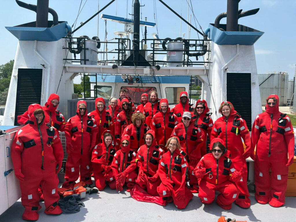 A group of teachers learn about survival suits on the Lake Guardian
