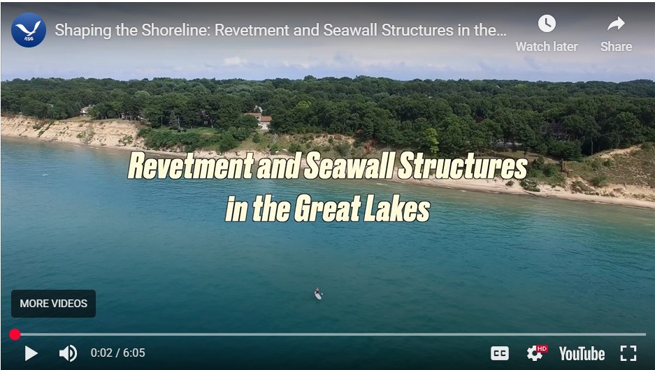 This image shows a head-on view of calm blue lake water as it meets the coastline. The coastline has steep beaches. There are many trees and two homes along the coast. The title, "Revetments and Seawall Structures" is displayed in text across the middle of the photo.